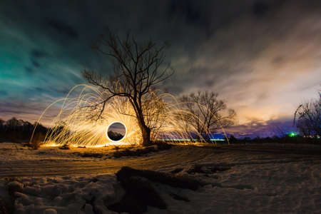 Abstract picture with trajectories of burning sparks near the tree at the background of spring night landscapeの写真素材