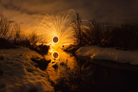 Abstract picture with trajectories of burning sparks on the surface creek at the background of spring night landscapeの写真素材