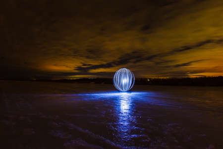 Futuristic glowing sphere on the surface of frozen lake at the background of spring night landscape