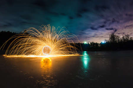 Trajectories of burning sparks on the surface of frozen lake at the background of spring night landscapeの写真素材