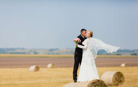 The bride and groom standing on haystack at the background of summer fieldの写真素材