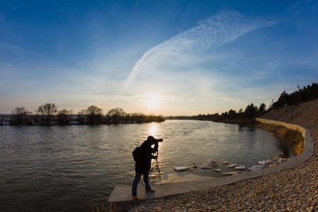 Professional photographer taking a photo flooding river at sunset standing at concrete protective structureの写真素材
