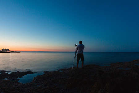 Photographer taking a photo of a beautiful sea view by his camera on a tripod