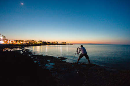 Photographer taking a photo of a beautiful sea view by his camera on a tripodの写真素材