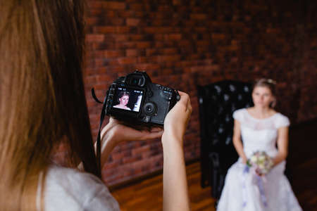 Photographer taking pictures the bride in the studio on a large leather armchairの写真素材