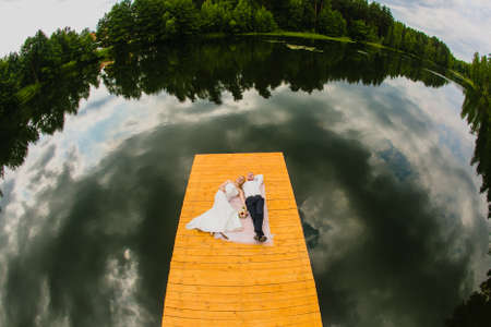 Couple of newlyweds and lake surface with reflect of cloudy skyの写真素材