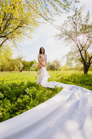 Young sexy brunette posing in a blooming garden with a long piece of white clothの写真素材