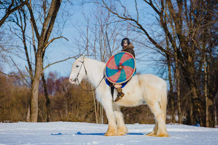 Man in suit of ancient viking riding big white horseの写真素材