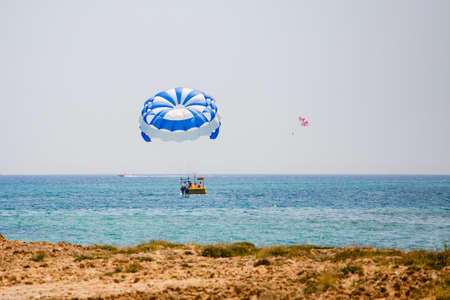 Parasailing water amusement - flying on a parachute behind a boat on a summer holiday by the sea in the resortの写真素材