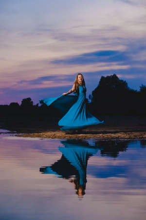 Beautiful blond model in blue air dress posing just near the sea edge