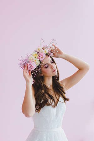 Young bride in white dress with flower wreath on her head posing in the studioの写真素材