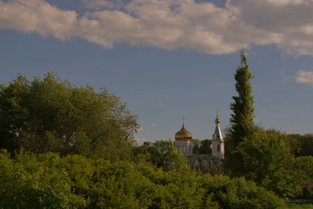 Gilded monastery domes among green trees against a blue sky with white cloudsの写真素材