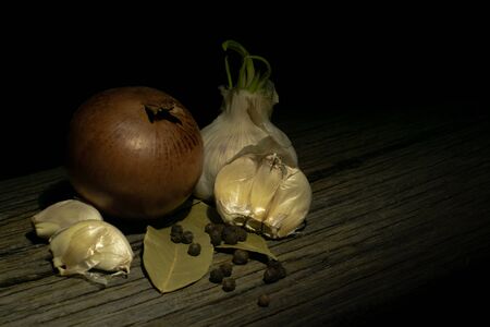 Onions, two heads of garlic, two cloves of garlic in the husk, peas and bay leaves on an old cracked tableの写真素材
