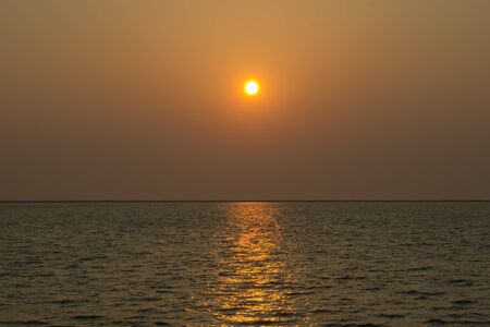 evening sun in a haze above the sea and sun glare on the waterの写真素材