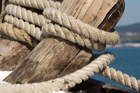 mooring rope superimposed on a wooden cracked bollard of an old sailing shipの写真素材