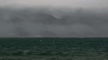 foggy morning, over the sea, waves with foamy scallops, mountains in the haze with clouds above themの写真素材