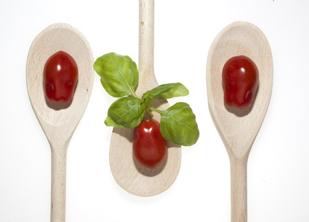 tomatoes basil on woodden spoon in white backgroundの写真素材