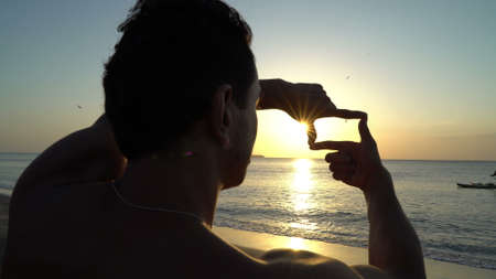 Man making photo frame by his hands over sunsetの写真素材