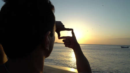 Man making photo frame by his hands over sunset