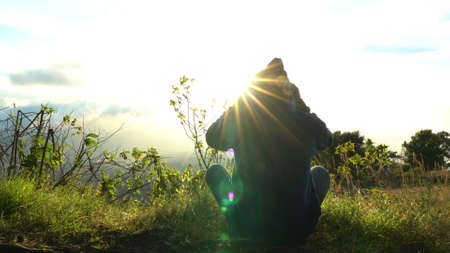 Man hermit meeting up sun rise on the edge of mountains. Doing meditation in sun light. Putting on hoodの写真素材