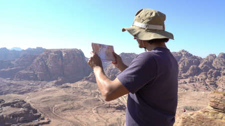 Hiker looking at map from mountain top Aerial shot of hiker looking at map from mountain top. Man reaches mountain peak, looks at map for directions.の写真素材