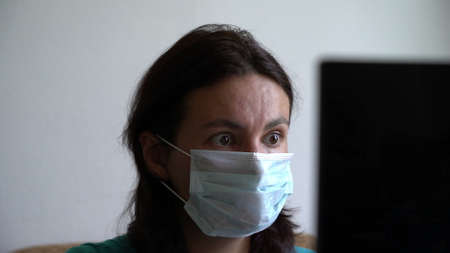 woman put on mask, reading new about pandemia of virus on laptop, looking scared shocked and...