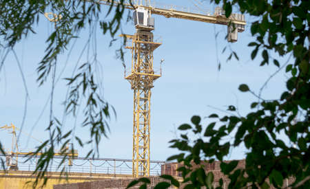 Construction site with cranes on the background of green trees and blue sky