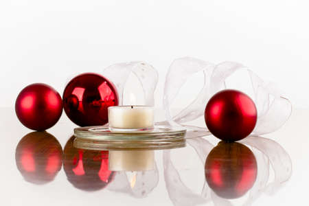 Christmas decoration of red flask white ribbon and a candle on a glossy surfaceの写真素材