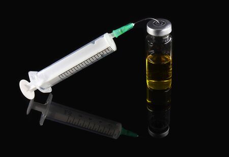 Syringe and glass bottle on black background