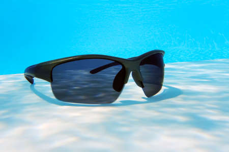 sunglasses in a blue pool of waterの写真素材