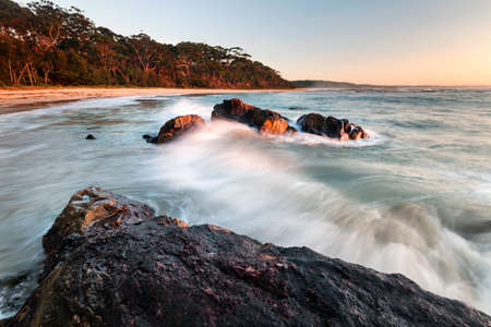 waves hitting rocks in the morning light at beachの写真素材