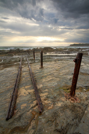 poles and rocks on coast at sunriseの写真素材