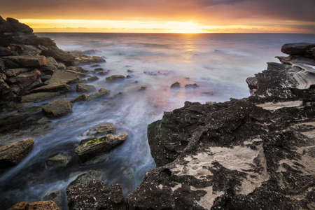 sunrise on the water and rocks on coastの写真素材