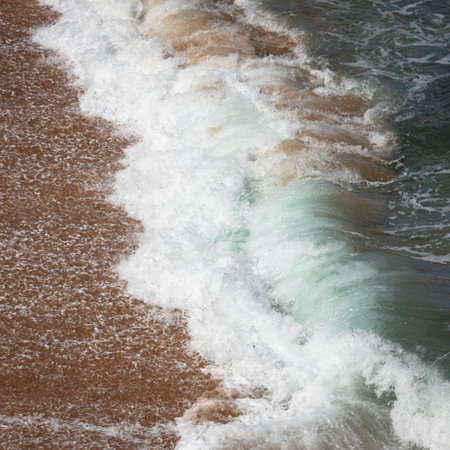 a wave from ocean crashing onto sand at the beachの写真素材