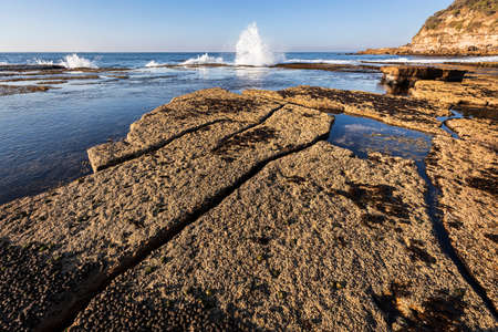 wave hitting rocks at the coast with calm water and clear blue skyの写真素材