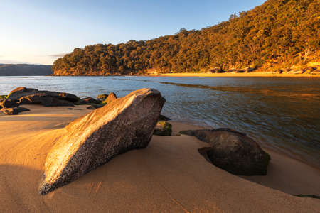 rocks on sandy beach near water with sunlight on headlandの写真素材