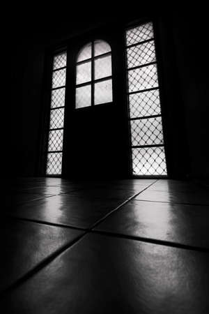 windows and a door in a dark room with light streaming onto tiled floorの写真素材