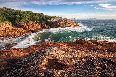 Waves on red rocks alongside ocean at broughton island near Hawks Nest in NSW Australiaの写真素材