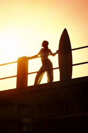Sihouette of young attractive surfer girl on beach pier with surfboard の写真素材