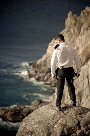 Handsome young man standing a top a rock with ocean below wearing climbing gearの写真素材