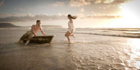 Happy young couple having fun with old vintage bath on the beach at sunriseの写真素材