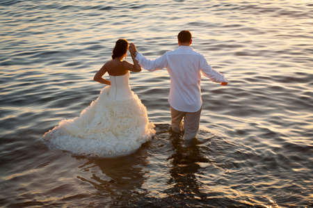 Beautiful couple walking into water with sunlight reflections of surfaceの写真素材