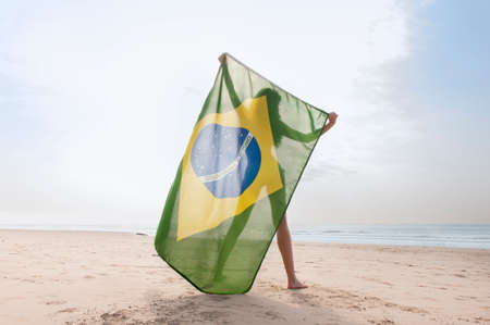 Young attractive woman in green bikini holding up Brazil flag on beachの写真素材