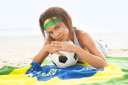 Young attractive mixed race girl on beach with Brazil flag and footballの写真素材