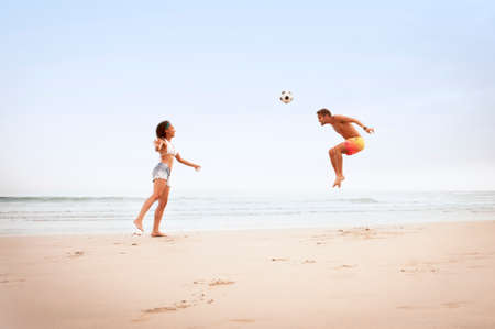 Young mixed race couple playing on beach with footballの写真素材