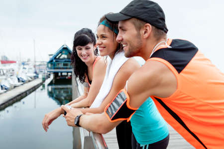 Group of happy runners relaxing and leaning on railing after morning exercise