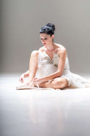 Young attractive ballerina sitting on the floor working with her pointed ballet shoesの写真素材