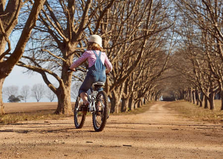 Young girl riding her bicycle bike down dirt road tree lined avenueの写真素材