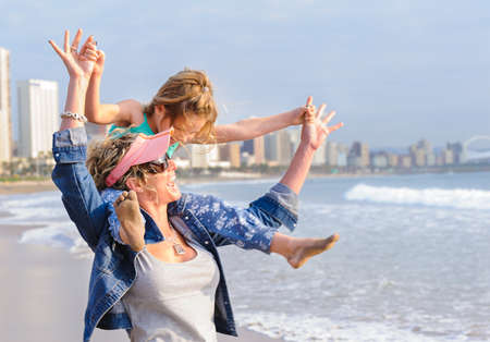 Young girl sitting on mom's shoulder while walking on beachfrontの写真素材