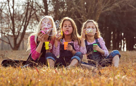 Young girls kids sisters blowing bubbles with soap in a farm fieldの写真素材
